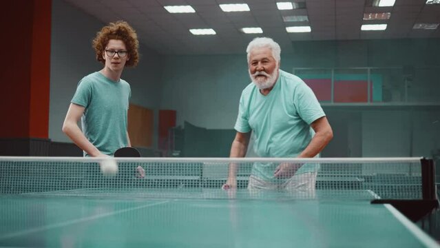 Teen grandson and his grandfather playing a doubles game of table tennis as one pair win and celebrate 