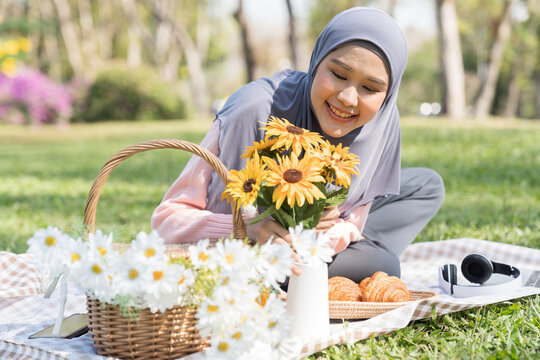 Asian young muslim woman wear hijab headscarf preparation yellow flowers put in vase with happy and smiling during picnic in park on holiday weekend