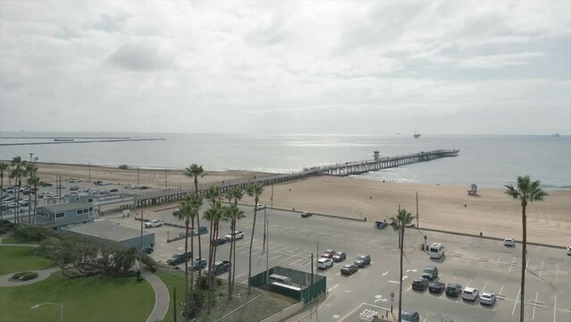 High-angle video panning over the nearly empty beach and Seal beach pier during a cloudy day