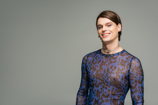 carefree pangender person in blue animal print top smiling at camera isolated on grey.