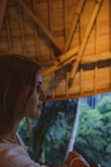 Vertical shot of the side of white female face with wooden ceiling and vegetation in the background