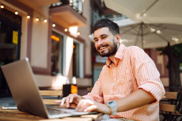 Smiling young man working in a cafe on the street with a laptop and phone. Freelance business concept. Business, blogging, freelancing, education concept. Modern lifestyle.