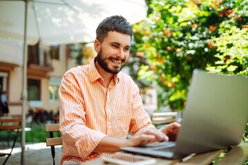 Smiling young man working in a cafe on the street with a laptop and phone. Freelance business concept. Business, blogging, freelancing, education concept. Modern lifestyle.