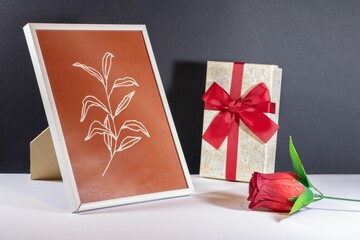 Closeup of a small jewellery gift box with an artificial rose and a photo frame on the table