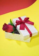 Vertical shot of a small jewellery gift box and an artificial red rose on a yellow surface