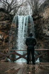 Vertical shot of a man standing in front of an amazing waterfall