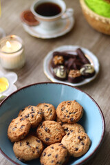 Easter eggs in the basket, bowl of cookies, chocolate pralines, Easter bunny figurine, cups of tea, glasses of juice, flowers and lit candles on the table. Selective focus.