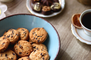 Easter eggs in the basket, bowl of cookies, chocolate pralines, Easter bunny figurine, cups of tea, glasses of juice, flowers and lit candles on the table. Selective focus.