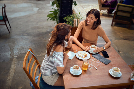 Young beautiful girlfriends having coffee at cafe. Chatting with each other and laughing.
