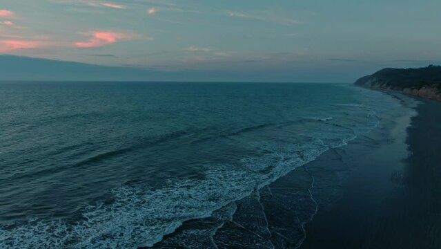 Aerial of calm sea waves rolling on an empty sandy beach at sunset in Ecuador.