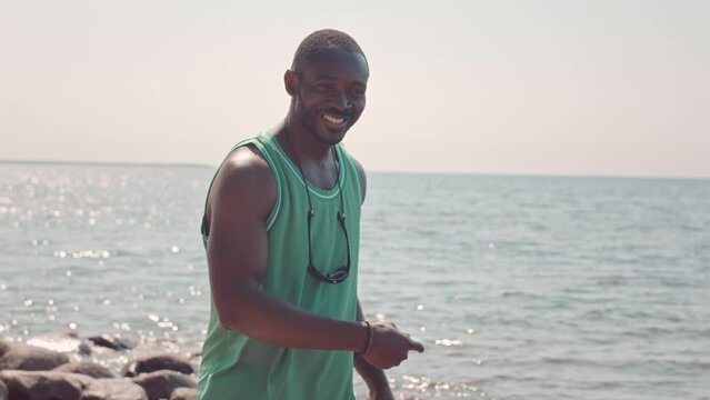Medium slowmo of happy young Black man throwing frisbee while playing with child at sandy beach on sunny day