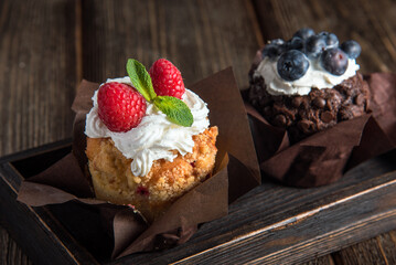 Muffins with cream, raspberries and blueberries on a wooden board. Close-up, side view.