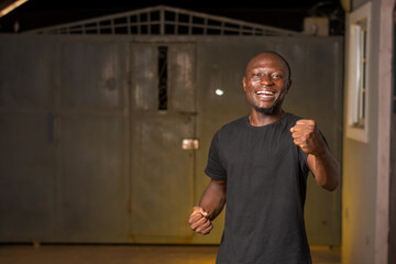 Happy young black African man raising his fist celebrating success, standing. giving good vibes