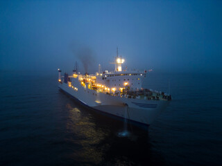 Aerial view of a ferryboat navigating through foggy conditions at night on the sea.