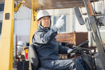 Fototapeta na wymiar Middle-aged Asian male worker with forklift on factory grounds.