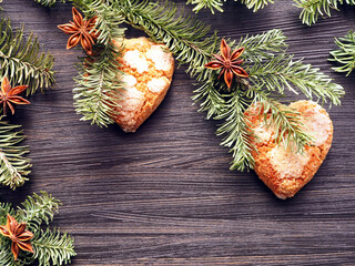Сookies in the shapes of hearts, decorated on fir branches with star anise on a dark brown wooden background
