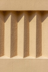 Beige exterior stucco wall with repeating details. Rough surface in the sun with shadows. Rough texture and background for design.