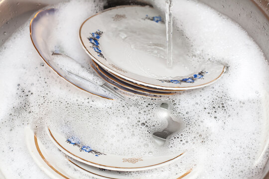 Composition about washing dishes. A set of large plates lie in the washbasin with foamy water. An image about housework, kitchen care and cleanliness.