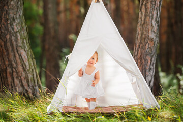 Little girl child is hiding in toy house tent outdoors. Summer sunny day.