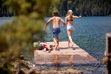 A young couple is jumping into the lake during mountain hiking. Trip, nature, hiking