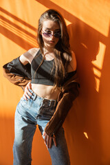 brunette in sunglasses stands on an orange background