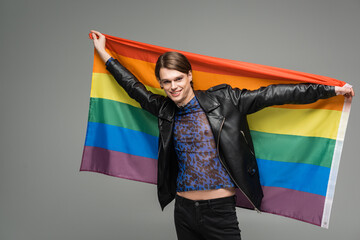 cheerful bigender person in black leather jacket posing with lgbt flag isolated on grey.