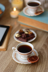 Books, reading glasses, e-reader, plate of chocolate pralines, bowl of cookies, cups of tea and lit candles on the table. Selective focus.