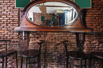 A mirror of a wooden frame dresser nailed to the brick wall of a bar with high stools