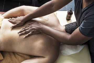 A brunette masseuse applying an oil massage on the back of a patient