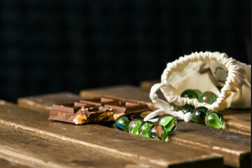  Image of glass marbles for children's games and a tablet of chocolate with hazelnuts on a wooden table