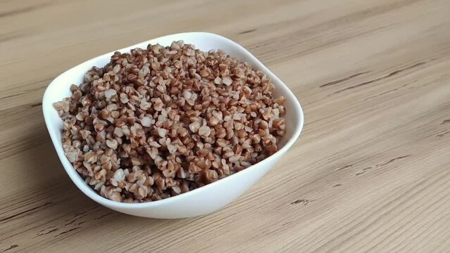 Boiled buckwheat porridge in a white ceramic plate on a brown wooden background
