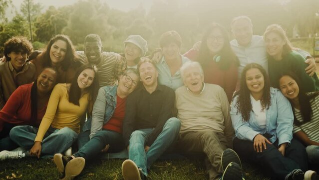 Happy multigenerational people with different ethnicity having fun sitting on grass in a public park