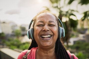 Happy African senior woman listening to music with wireless headphones while smiling into the camera