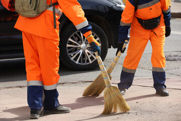 Two janitors in orange uniform sweeping the street on car background. Cleaning spring city