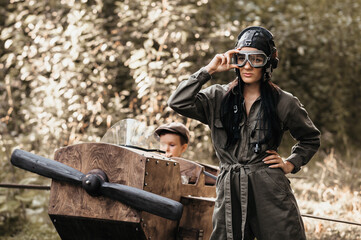 A young aviator boy sits in a homemade airplane in a natural landscape. Next to her is an aviator mom in a helmet and glasses. The authentic mood of the picture. . Cartography. Vintage.