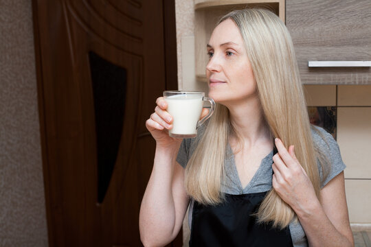 Adult blonde woman drinks a glass of fresh milk in the kitchen. An image for your healthy food creatives.