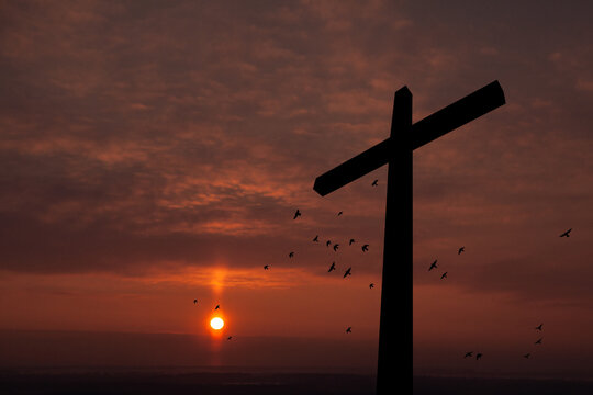 Christian cross with flying birds at sunrise. Resurrection of Jesus. Concept photo.