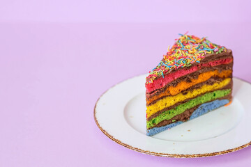 Rainbow birthday cake decorated with a festive candle and confetti. Confectionery. Multicolored dessert in the color of the rainbow on a purple background.
