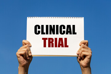 Clinical trial text on notebook paper held by 2 hands with isolated blue sky background. This...