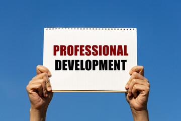 Professional development program text on notebook paper held by 2 hands with isolated blue sky background. This message can be used as business concept about professional development.