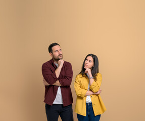 Uncertain young couple with hands on chins thinking for solution. Serious young man and woman...
