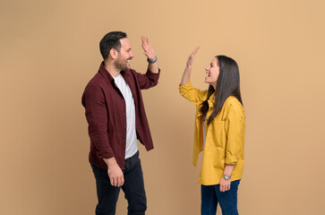 Ecstatic man and woman screaming and giving high five to each other while celebrating success. Excited young couple clapping hands and greeting while standing over yellow background - Powered by Adobe