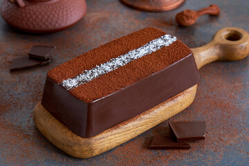 Dark chocolate milk pudding cake with cocoa powder and coconut flakes topping served on wooden...