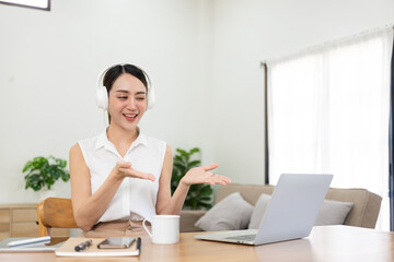 Pretty Asian girl in headphones listening to music happily on her laptop and mobile. Enjoy listening to music at work during vacation, work from home concept.