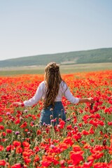 Obraz na płótnie Canvas Happy woman in a poppy field in a white shirt and denim skirt with a wreath of poppies in her hand posing and enjoying the poppy field.