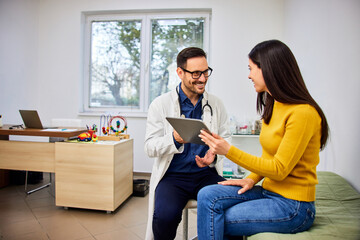 A smiling doctor uses a tablet to explain a child's health condition to a mother.