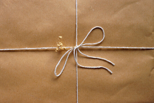 Present wrapped in recycled brown paper with white ribbon and dry gypsophila flowers. Sustainably wrapped gift on wooden background. Top view.