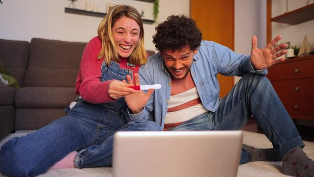 young happy couple having a video call to show their family the positive pregnancy test. husband and wife having a conference on the laptop explaining to their friends that they are waiting for a baby