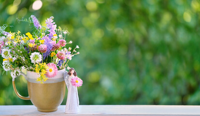 angel figurine and flowers bouquet in cup on table, abstract green natural background. Religious church holiday. symbol of faith in God, christianity. Happy Name Day greeting card design. copy space