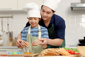 Happy smiling Asian father and son kid with apron and chef hat cooking meal together at kitchen,...